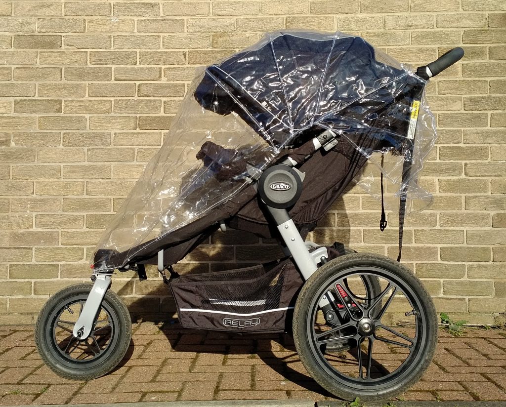 Graco Relay Pushchair with fitted rain cover against a brick wall
